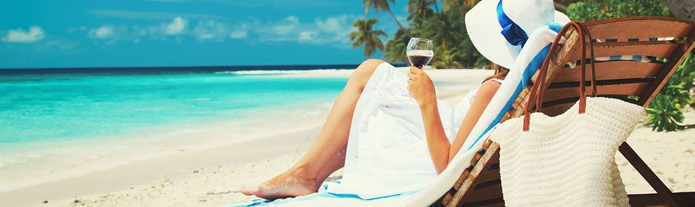 O femeie la plajă, pe un șezlong cu un pahar de vin