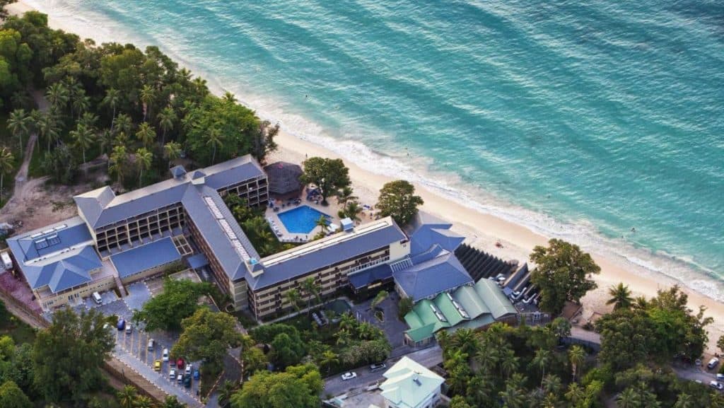 Vedere panoramică aeriană a unui resort situat pe o coastă din Seychelles cu apă turcoaz și nisip alb.