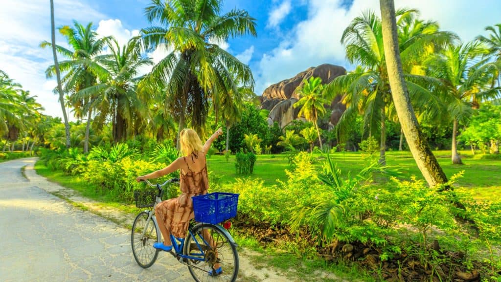 Femeie plimbându-se cu bicicleta pe o strada înconjurată de vegetație naturală verde din Seychelles.