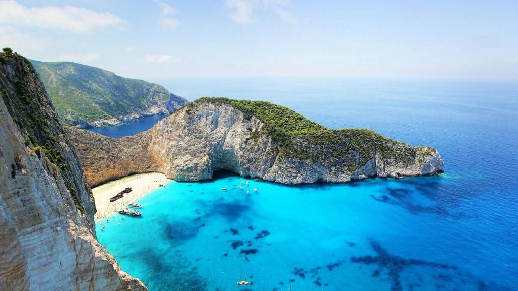 Vedere panoramică a plajei Navagio înconjurată de stânci uriașe și apă turcoaz.