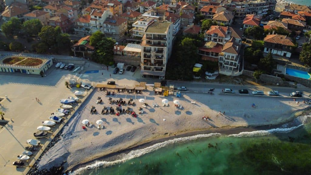 Zonă de coastă din Pomorie cu nisip fin și clădiri alăturate.