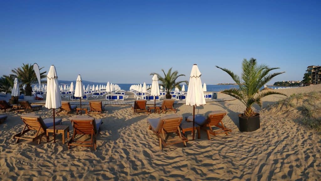 Șezlonguri de lemn pe o plajă cu umbrele albe din Sunny Beach