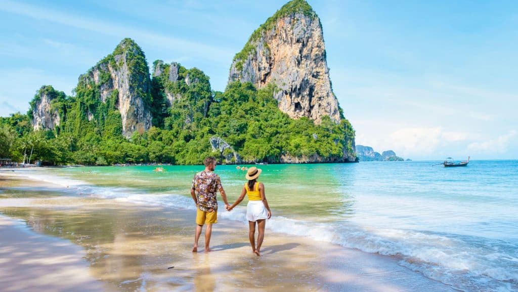 Un cuplu plimbându-se pe lângă apă pe plaja Railay din Krabi, Thailanda