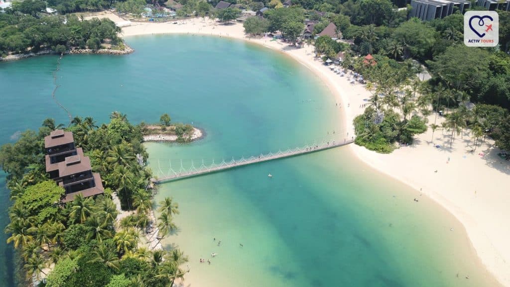 Peisaj panoramic al unei plaje conectate la o insula cu un pod lung.